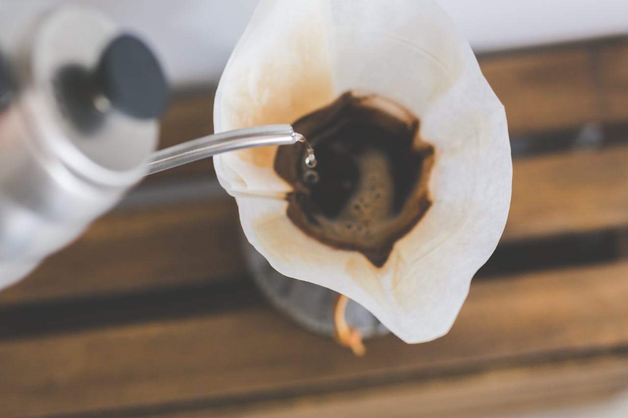 Close-up of pour over coffee brewing with filter paper and kettle pouring hot water.