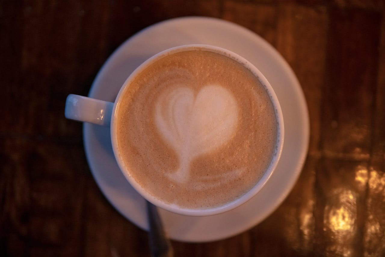 A close-up of a latte with heart-shaped foam art, captured on a wooden table.